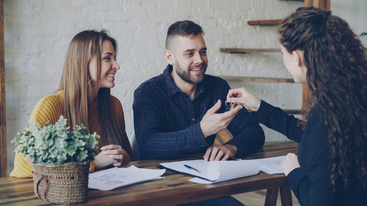 A couple and an agent going through documents at a table as keys are handed over
