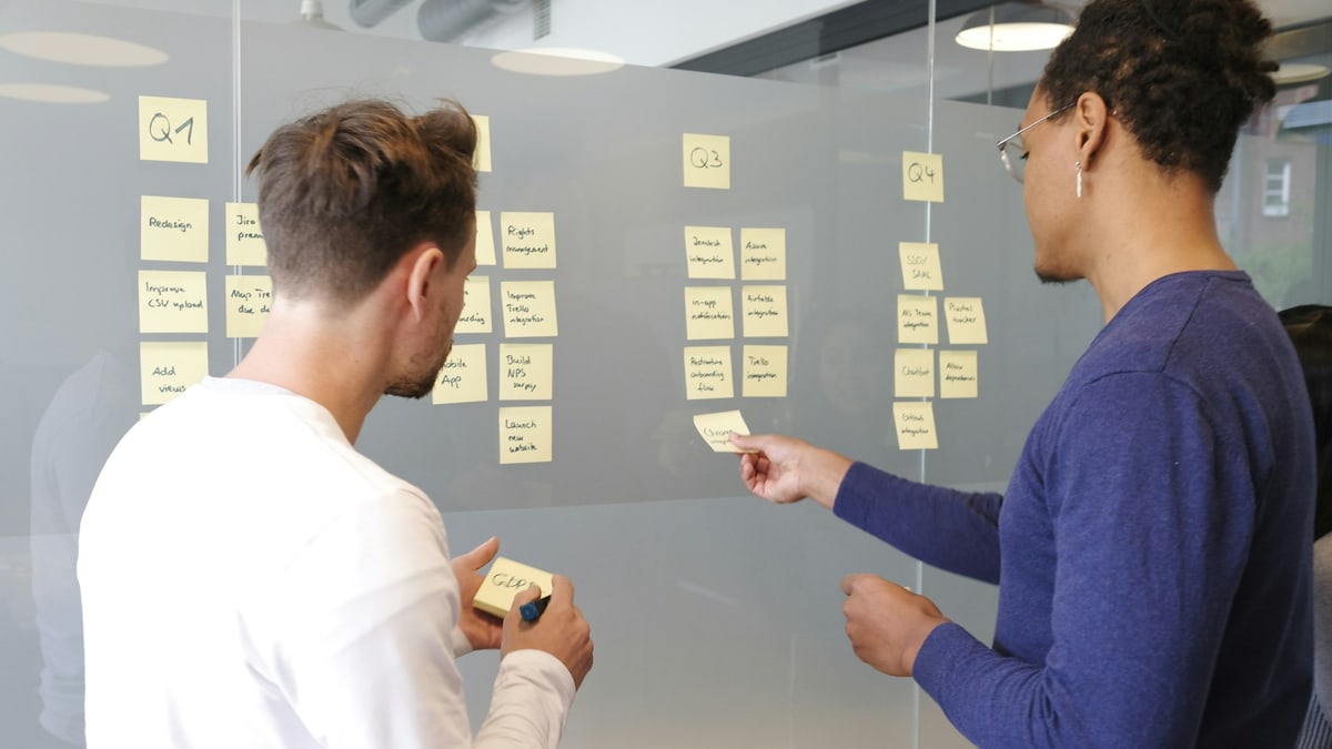 Two colleagues planning a campaign with sticky notes arranged on a glass wall