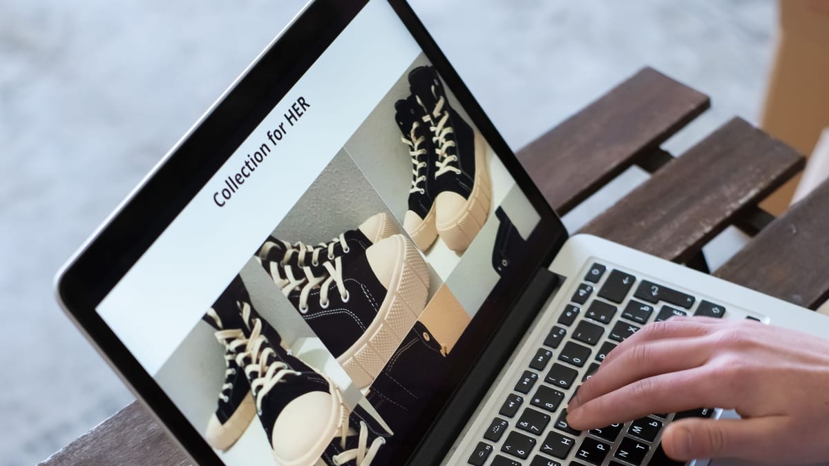 A person typing on a laptop that shows an online store page of sneakers