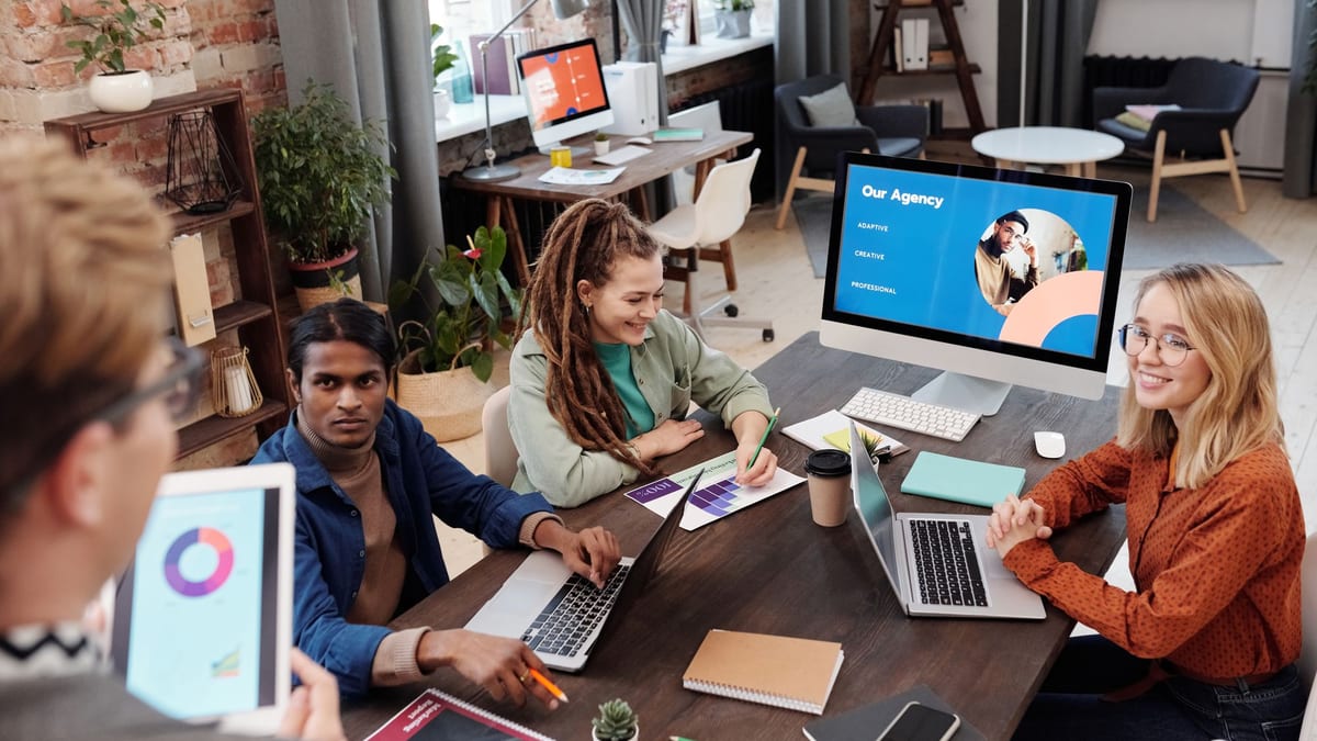 A team around a table with laptops, a tablet and a monitor showing an agency presentation