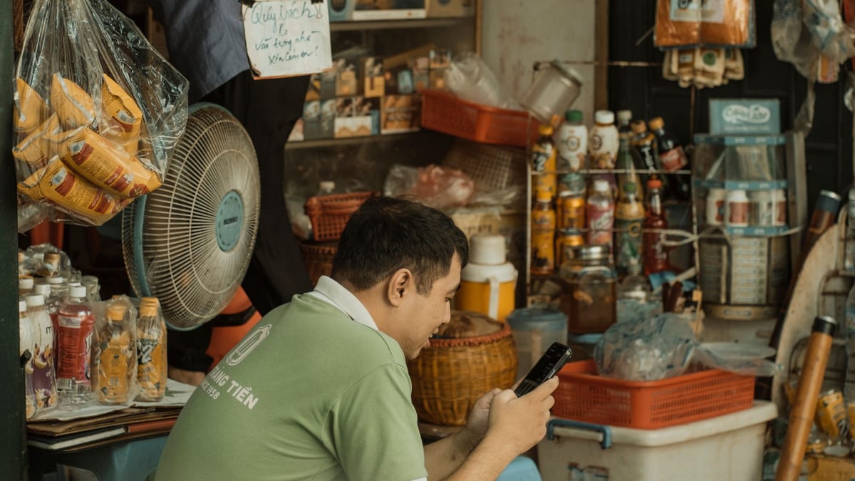 A man in a market stall checking his phone among shelves of goods