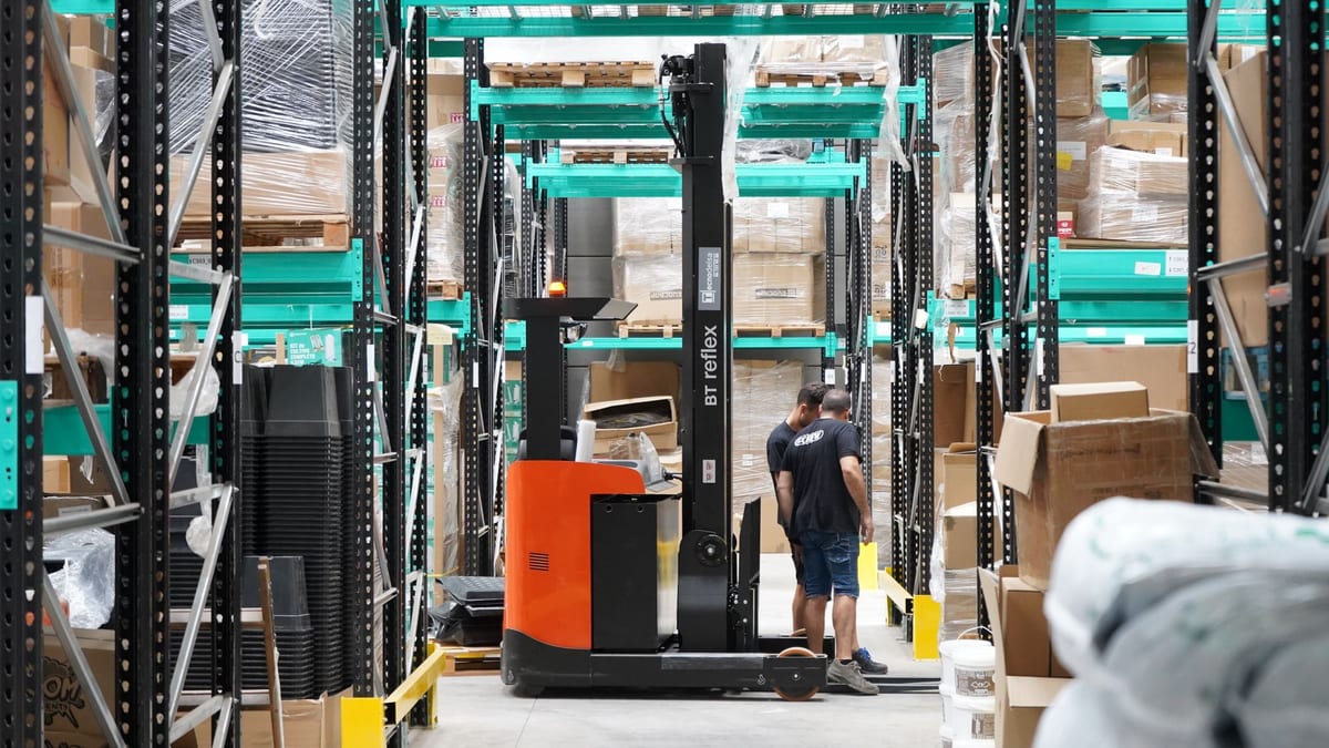A forklift and a worker in a warehouse aisle between tall shelving
